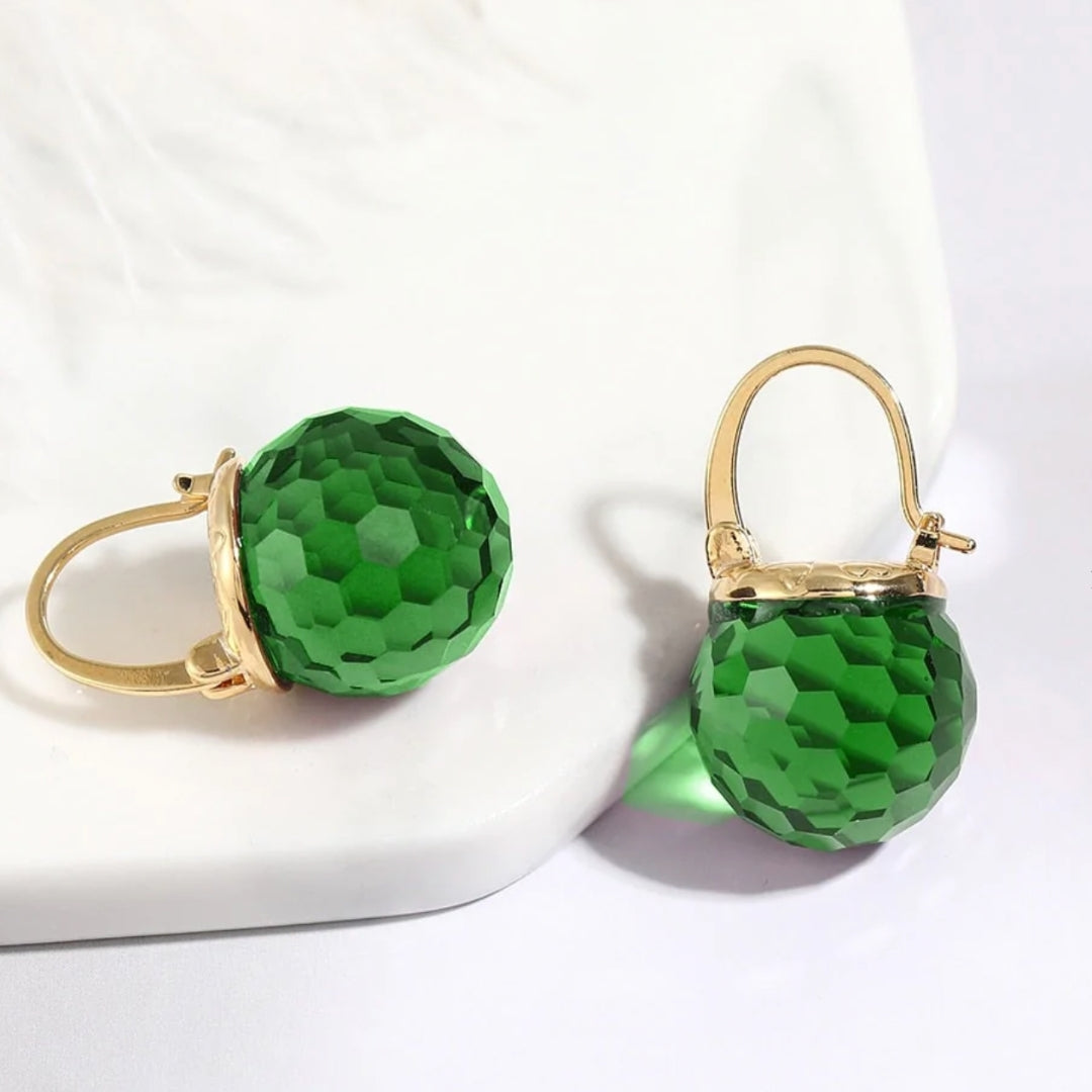 A pair of green crystal earrings with gold accents, displayed on a white surface.