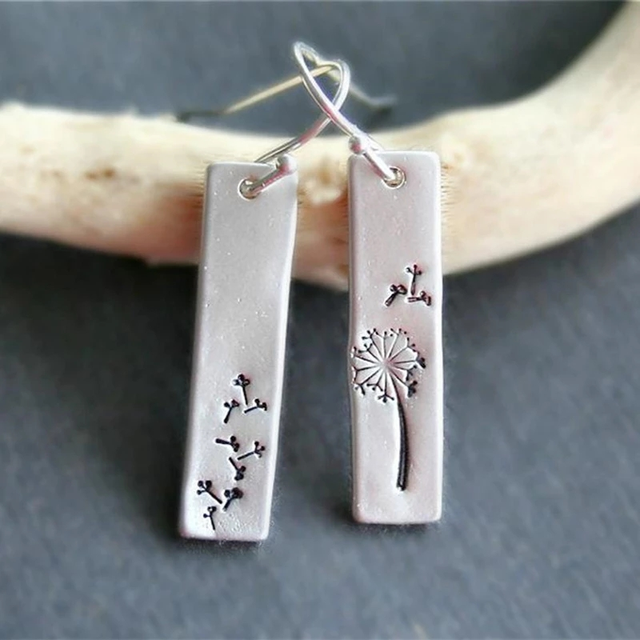 Shop our Vintage Dandelion Rectangular Earrings—engraved silver with one full bloom and one scattered seeds—displayed on curved wood. Handcrafted and available now during our exclusive jewelry sale.