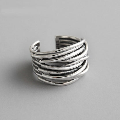The 925 Sterling Silver Adjustable Layered Ring features overlapping, curved bands in a stunning handcrafted design. This open-ended silver ring is showcased on a plain, light gray background.