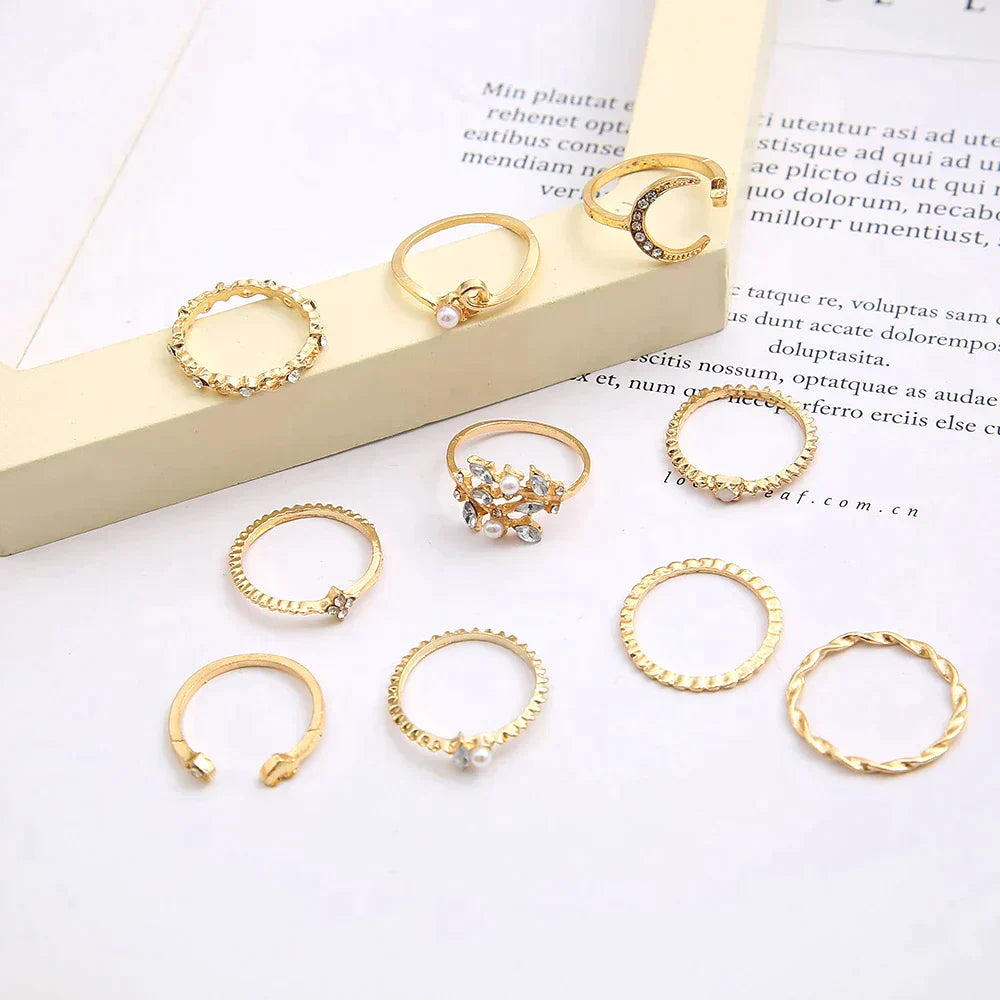 A 10 pack of Bohemian silver and gold plated rings with various textures and designs, featuring pearls and small stones, arranged on a white surface with a beige frame in the background.