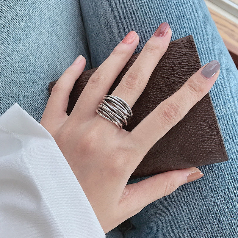A hand with neatly manicured nails wears our 925 Sterling Silver Adjustable Layered Ring and holds a textured brown wallet, styled with blue jeans and a white shirt.