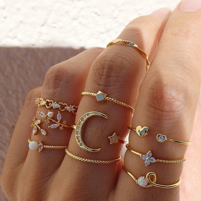 A hand stylishly displays the 10 Pack of Bohemian Silver and Gold Plated Rings, each featuring crescent moons, stars, hearts, gemstones, and delicate patterns, creating a trendy layered look with high quality handcrafted jewelry.
