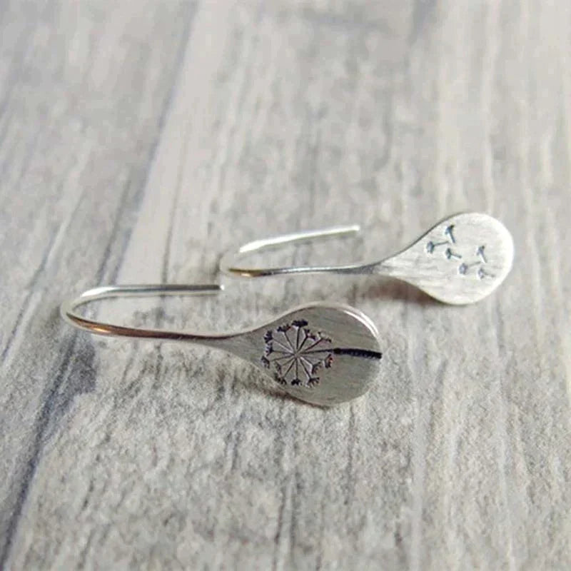 A pair of 925 Sterling Silver Dandelion Leaf Earrings with engraved dandelion designs on flat, rounded ends, displayed on a wooden surface.
