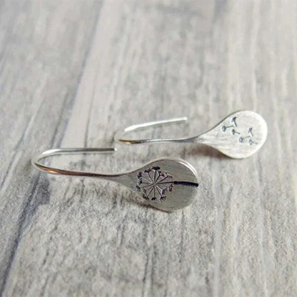 A pair of 925 Sterling Silver Dandelion Leaf Earrings with engraved dandelion designs on flat, rounded ends, displayed on a wooden surface.