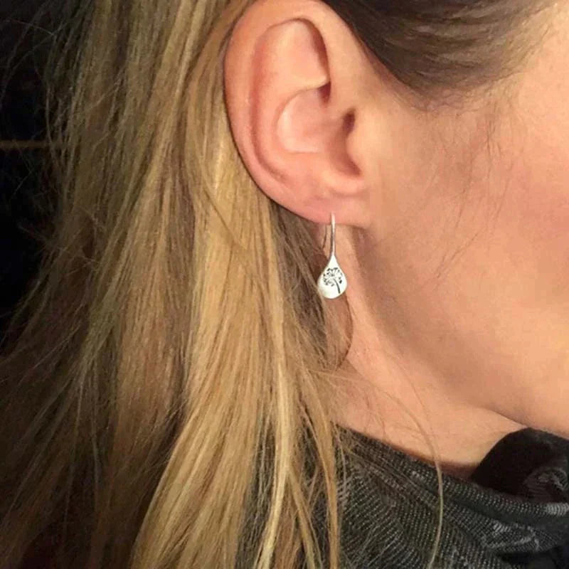 Close-up of a woman's ear with long blonde hair, wearing 925 Sterling Silver Dandelion Leaf Earrings, handcrafted and engraved with a delicate design, set against a dark background.
