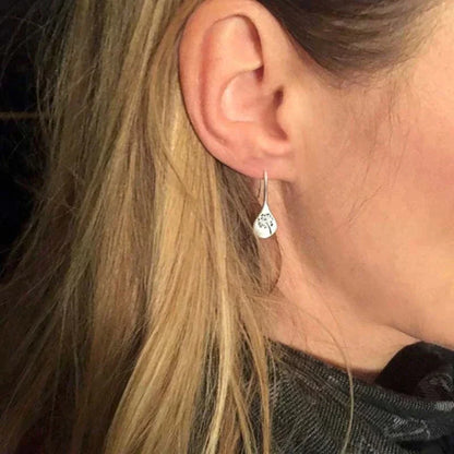 Close-up of a woman's ear with long blonde hair, wearing 925 Sterling Silver Dandelion Leaf Earrings, handcrafted and engraved with a delicate design, set against a dark background.