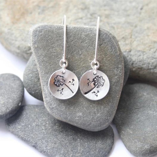Vintage Rounded Dandelion Earrings—silver dangle earrings with round pendants engraved with a wind-blown dandelion, displayed on smooth gray stones; perfect handcrafted jewelry.