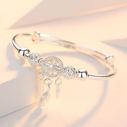 The 925 Silver Adjustable Dreamcatcher Bracelet features a central dreamcatcher charm with three feather charms and two decorative beads, all handcrafted and displayed on a soft pastel background.