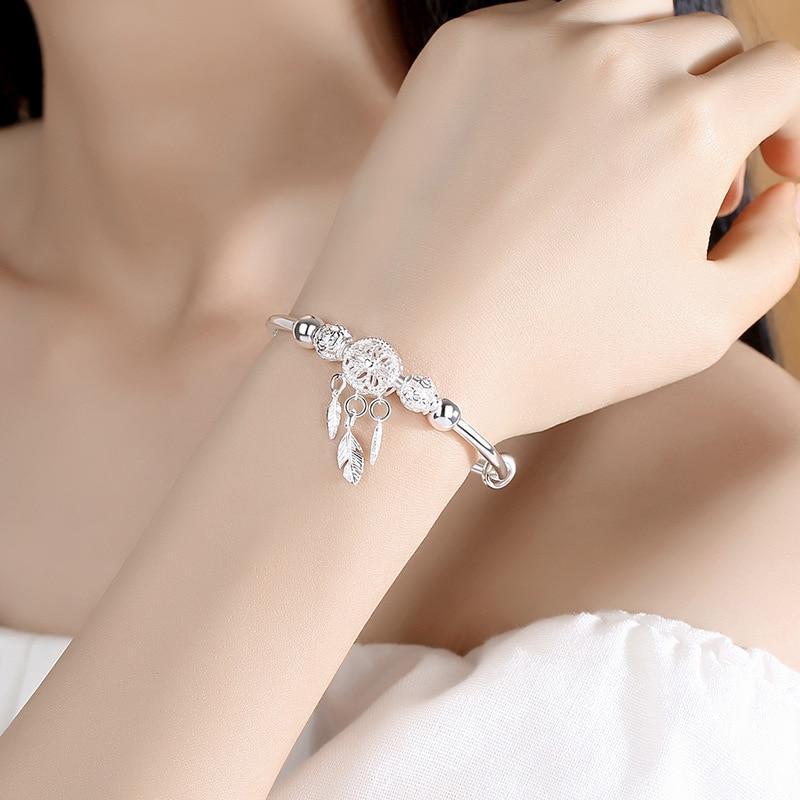 A close-up of a woman's arm wearing the 925 Silver Adjustable Dreamcatcher Bracelet, featuring a delicate dreamcatcher charm and feather pendants, showcases the elegance of this high-quality jewelry against a soft, neutral background.