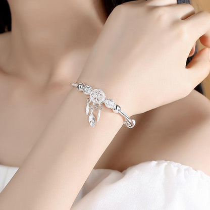 A close-up of a woman's arm wearing the 925 Silver Adjustable Dreamcatcher Bracelet, featuring a delicate dreamcatcher charm and feather pendants, showcases the elegance of this high-quality jewelry against a soft, neutral background.